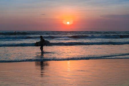 People bathing in the sun in sunset, swiming and playing games on the beach. Tourists on the sand beach in Bali, Indonesiaの写真素材