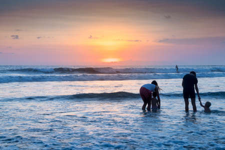 People bathing in the sun in sunset, swiming and playing games on the beach. Tourists on the sand beach in Bali, Indonesiaの写真素材