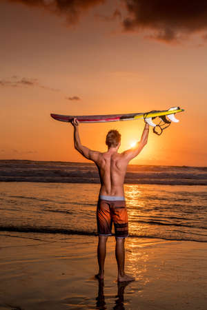 Surfer on the beach holding surfobard at the sunset in Bali, Indonesiaの写真素材