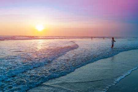 People bathing in the sun in sunset, swiming and playing games on the beach. Tourists on the sand beach in Bali, Indonesiaの写真素材