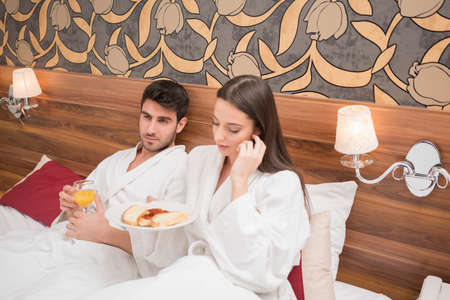 Attractive young couple in white robes, enjoying food and drink in bad after spa.Couple in relationship love and careの写真素材