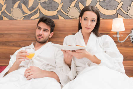 Attractive young couple in white robes, enjoying food and drink in bad after spa.Couple in relationship love and careの写真素材