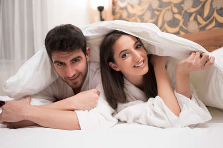 Beautiful happy young couple enjoying in bed after spa. Couple in white robes relaxingの写真素材