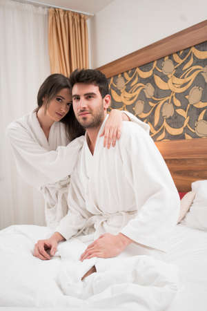 Beautiful happy young couple enjoying in bed after spa. Couple in white robes relaxingの写真素材