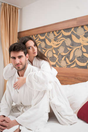 Beautiful happy young couple enjoying in bed after spa. Couple in white robes relaxingの写真素材