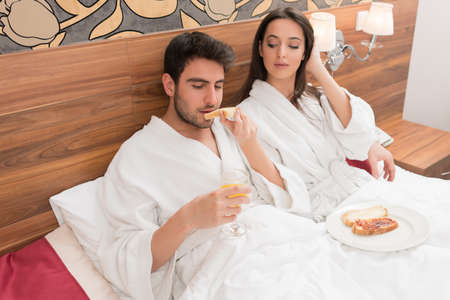 Attractive young couple in white robes, enjoying food and drink in bad after spa.Couple in relationship love and careの写真素材