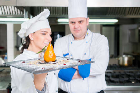 Two Famous Chefs holding Their delicious dessert. They Work on a Big Restaurant Stainless Steel...