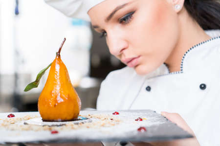 Beautiful young woman chef in white uniform preparing decorating delicious dessert in restaurant...