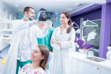 Dental medical team examining and working on young Â¸female patient.Dentist's office, while technician is reviewing xray.の写真素材