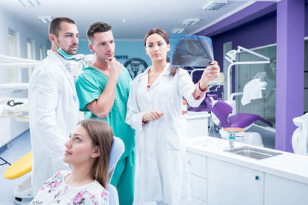 Dental medical team examining and working on young Â¸female patient.Dentist's office, while technician is reviewing xray.の写真素材