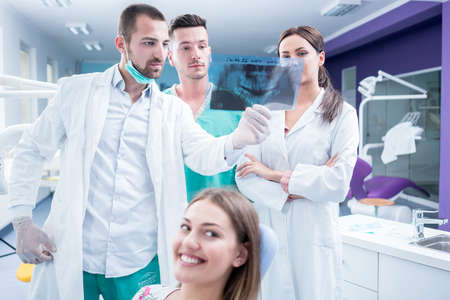 Dental medical team examining and working on young Â¸female patient.Dentist's office, while technician is reviewing xray.の写真素材