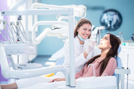 people, medicine, stomatology and health care concept - happy female dentist with mirror checking patient girl teeth up at dental clinic officeの写真素材