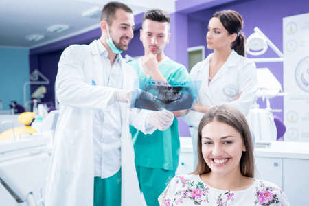 Dental medical team examining and working on young Â¸female patient.Dentist's office, while technician is reviewing xray.の写真素材