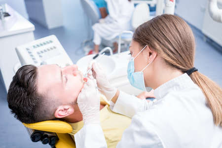 people, medicine, stomatology and health care concept - happy female dentist with mirror checking patient man teeth up at dental clinic office.の写真素材