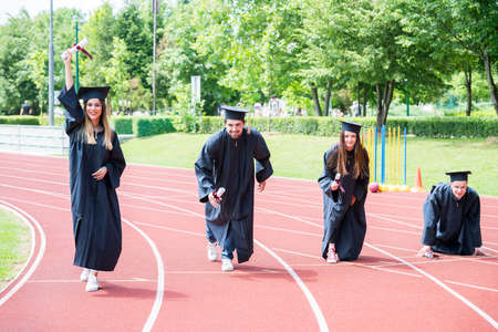 Graduation group of students celebrating on athletic track, preparing to race. Students competiting in a race on athletic track after graduating.の写真素材
