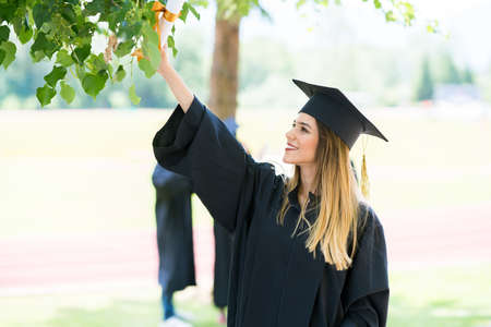 Graduation: Student Standing With Diploma With Friends Behindの写真素材