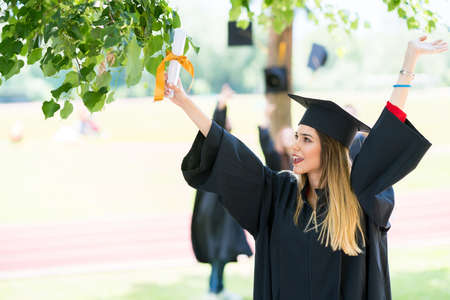 Graduation: Student Standing With Diploma With Friends Behindの写真素材