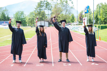 Graduation group of students celebrating on athletic track with diplomas raised high.の写真素材