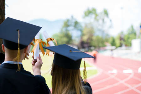Group of graduate students from behind. Students holding diplomas with a view on athlete trackの写真素材