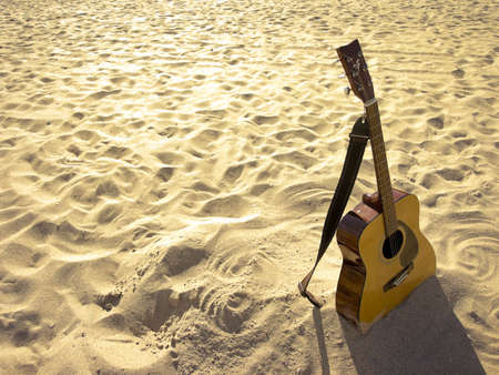 An acoustic guitar standing in the sandy beach.の写真素材