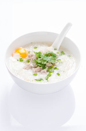 cangee or rice gruel with minced pork and egg in white bowl and spoon on white background and reflectionの写真素材