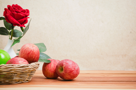 red apples in basket on wood table, looks healthy and dietary decore with rose vaseの写真素材