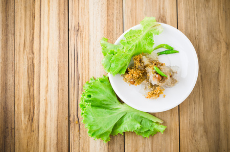 Thai dessert, steamed-rice filled with minced pork topped with fried garlic prepared with green chilli pepper and vegetable put in white dish on wood tableの写真素材