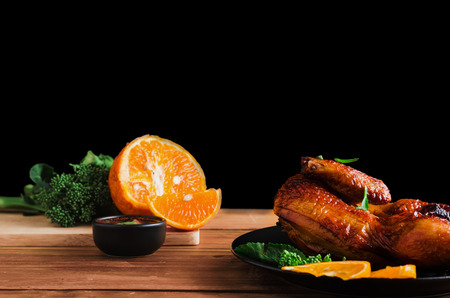 chicken grilled on plate with black background and wood table prepared with spicy dipping, orange fruit and vegetableの写真素材