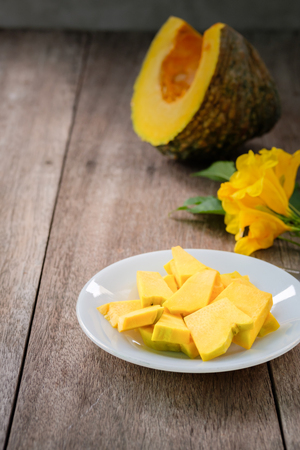 cucurbita pepo or pumpkin is cut and put on a white plate on old wood table beside the yellow flower, edible fruit or vegetable, iincluding beta-cryptoxanthin, alpha and beta caroteneの写真素材
