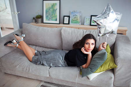 Armenian brunette girl lies on a sofa with a balloon in the shape of a star. Comfortable interiorの写真素材
