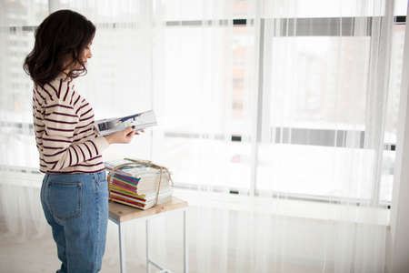 Armenian girl in a sweater and jeans reading a magazine at the table with magazines. Against the...