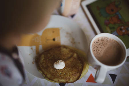 The baby eats pancakes with sour cream and cocoa. Close up.