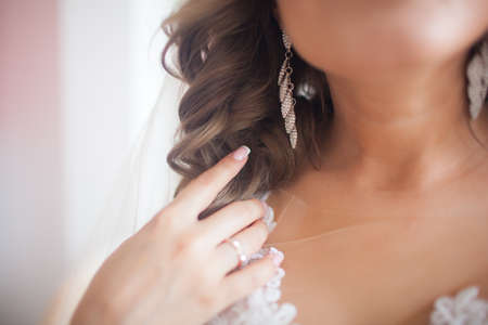 A young woman touches her wedding earrings with her hands.