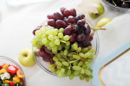 Multicolored grapes in a beautiful plate on a light background. Close up.