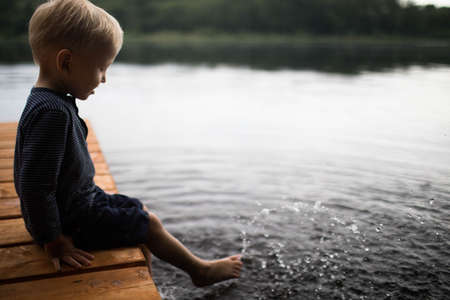 A little blond boy dips his feet in the pond.の写真素材