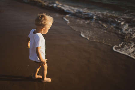 A little blond boy runs around cheerful on the beach. A beautiful wave.