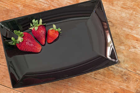 three red strawberries in a black plate and wooden baseの写真素材