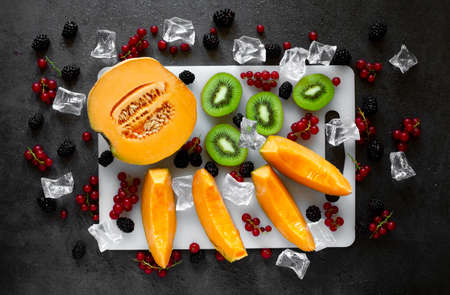 top view cutting board with fresh fruit on dark gray background with cold water drops and ice cubesの写真素材