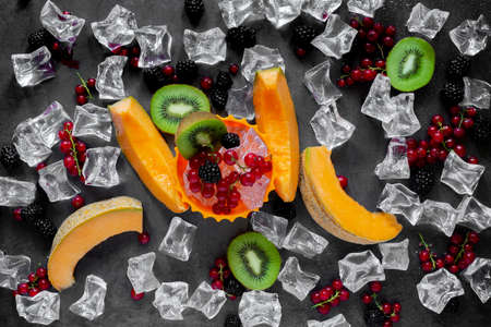 top view cutting board with fresh fruit on dark gray background with cold water drops and ice cubesの写真素材