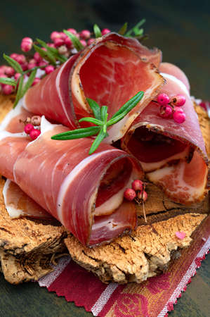 Slices of Alto Adige speck rolled with wild red pepper on a cork plateの写真素材
