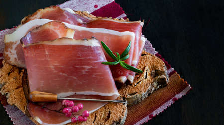 Slices of Alto Adige speck rolled with wild red pepper on a cork plateの写真素材