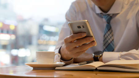 Male hand holding ready to make note, looking at cellphone. Businessman or employee at workplace writing business ideas, plans or tasks at personal organizer.の写真素材