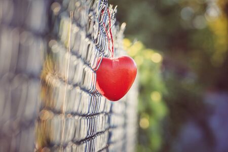 Love concept, heart shape love symbol hanging on grid fence in vintage and grainy styleの素材