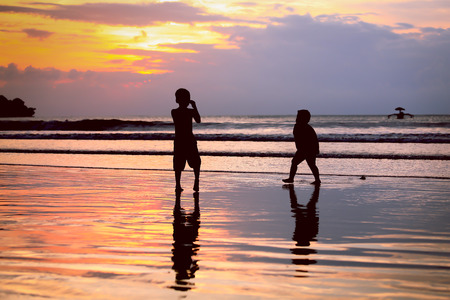 Golden sunset and group of kids enjoy playing on the beach with sun rays sky at Jimbaran beach, Indonesiaの写真素材