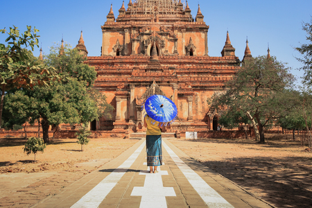 Back side of burmese woman holding traditional blue umbrella walking at temple in Bagan, Myanmarの写真素材