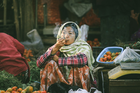 BAGAN, MYANMAR - Fabruary 3, 2017 : Burmese vendor smoking a traditional cigar while selling fresh vegetables in the marketのeditorial素材