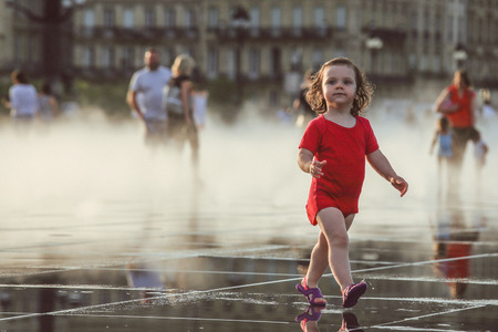 BORDEAUX, FRANCE - 3 April, 2017 : Little girl enjoy walking at Bordeaux water mirror in the hottest day during the sunset with water splash, grain texture style applyのeditorial素材