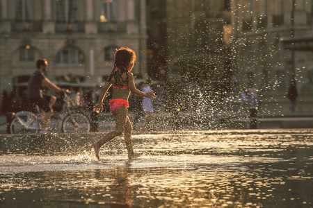 BORDEAUX, FRANCE - 3 April, 2017 : Little girl enjoy walking at Bordeaux water mirror in the hottest day during the sunset with water splash, grain texture style applyのeditorial素材