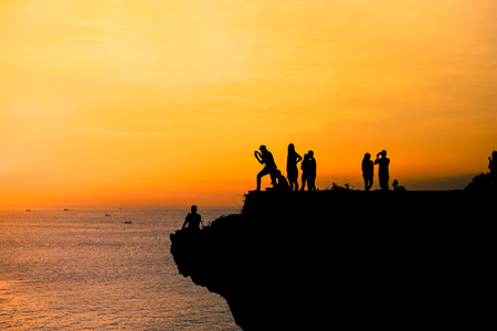 Silhouette of people taking picture on the cliff during the sunsetの写真素材