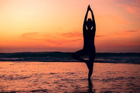 Meditation yoga silhouette of woman on the sea beach at sunset.の写真素材